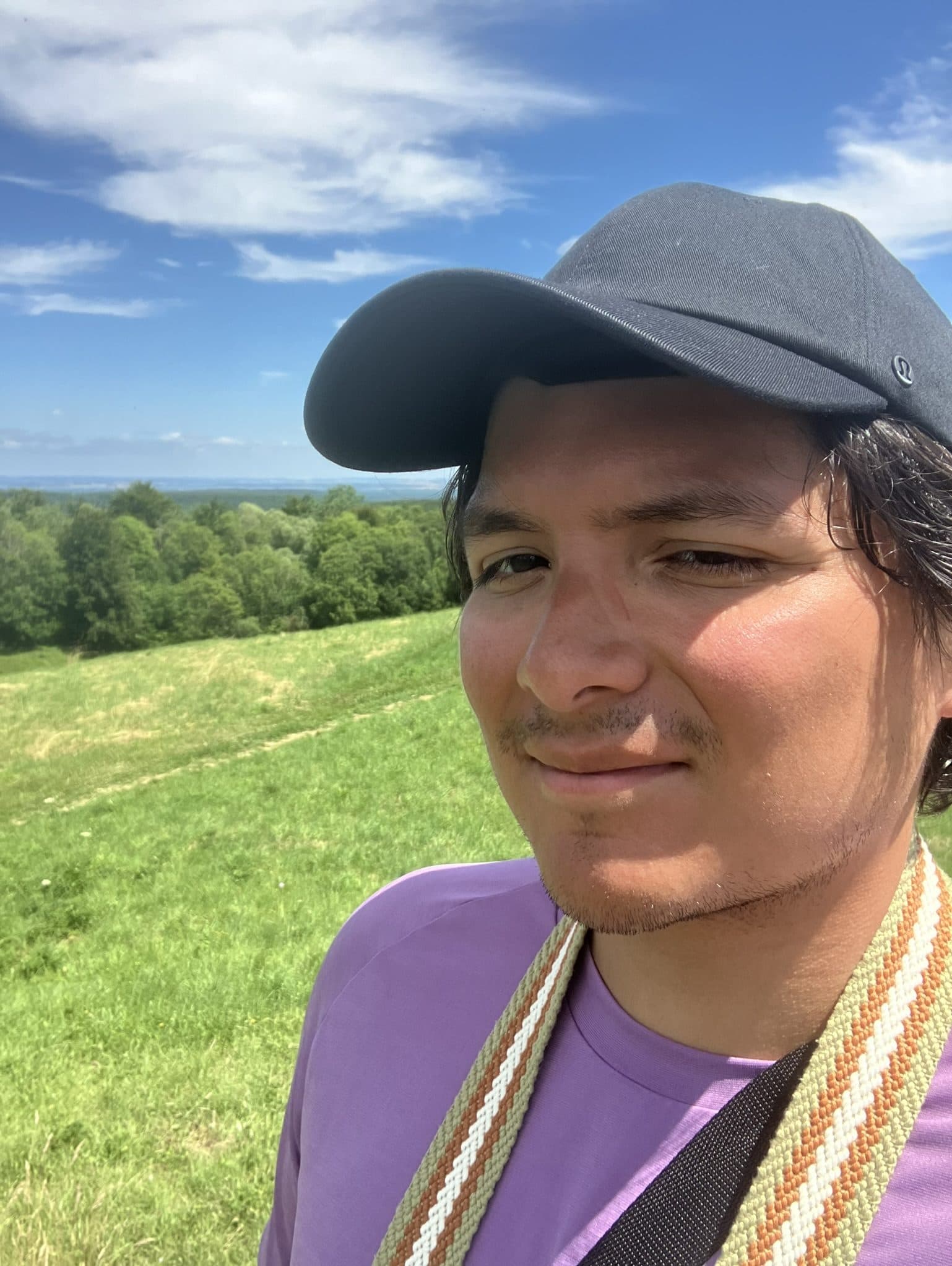 Emmanuel Mendieta squinting into the sun on a green hillside